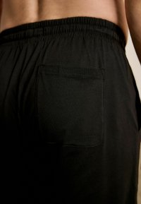 Pantaloni cu talie elastică neagră, dintr-un material moale, având un buzunar la spate. Design simplu, fără modele sau accente suplimentare.