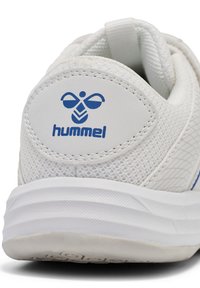 Talons de chaussure de sport blanche avec logo "hummel" bleu et un dessus en tissu en maille rembourré, présentant une semelle en caoutchouc blanc texturé.