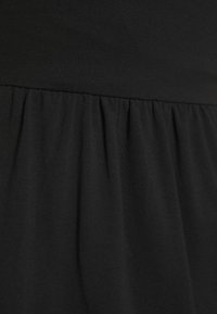 Lähikuva kerätyn mustan kankaan yksityiskohdasta, joka näyttää tekstiilin rakenteen ja ompelun vaatteessa.