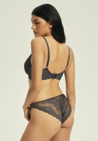 Szary stanik koronkowy i pasujące stringi, z misternymi wzorami, regulowanymi ramiączkami oraz zapięciem na haczyk z falbaniastymi krawędziami z tyłu.