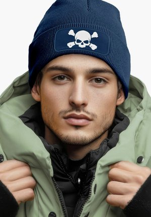 Navy knit beanie featuring a white skull and crossbones graphic, paired with a green insulated jacket, highlighting textured fabric details.