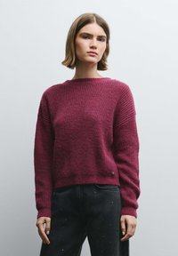 Suéter de punto burdeos con patrón texturizado y puños acanalados, con cuello redondo y un pequeño logo en el dobladillo.