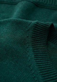 Pull en maille vert foncé avec col côtelé et texture lisse, avec des coutures discrètes le long des coutures.