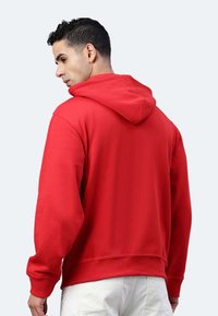 Felpa con cappuccio rossa caratterizzata da un colore solido, maniche lunghe e una vestibilità rilassata. Il tessuto sembra morbido con polsini e orlo a costine.