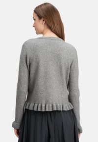 Grauer gestrickter Pullover mit langen Ärmeln, mit einem gerippten Saum und subtiler Textur. Ansicht von hinten, kombiniert mit einem dunklen Rock.