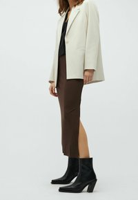 Blazer beige, top nero, gonna midi ribbed marrone con spacco laterale, stivali neri alla caviglia con punta squadrata e tacco spesso.