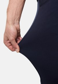 Granatowy, elastyczny materiał ubraniowy ciągnięty ręką, co ukazuje jego elastyczność. Materiał wydaje się gładki i dopasowany do ciała.