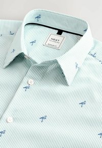 Camisa a rayas verde claro con bordado de flamenco azul, con cuello clásico y botones blancos. Etiqueta de Next Tailoring visible.