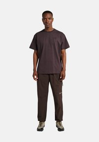 Ciemnobrązowa koszulka z okrągłym dekoltem i krótkimi rękawami, zestawiona z ciemnobrązowymi spodniami z teksturowanej tkaniny i boczną kieszenią.