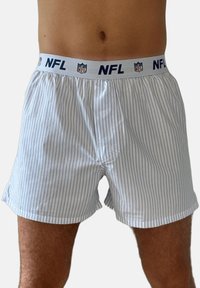 Männlicher Oberkörper, bekleidet mit weißen Boxershorts mit dünnen blauen vertikalen Streifen und einem weißen Bund mit dem NFL-Logo und Text.