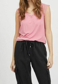 Rosa ärmlös topp med spetsdetalj och V-ringning, kombinerad med svarta cargobyxor med dragsko och sidofickor.