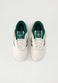 Bijele kožne tenisice s zelenim akcentima, perforiranim prednjim dijelom i tri zelene pruge. Imaju bijele vezice i podstavu od zelenog punjenja.