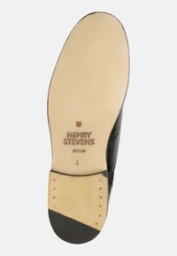 Schwarze Ledersohle mit einer glatten beigen Oberfläche, markiert mit "HENRY STEVENS BERLIN", verziert mit goldenen Nieten und einer abgerundeten Kante.