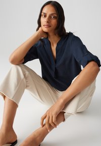 Top in lino blu navy con scollo a V e maniche arrotolate, abbinato a pantaloni cropped off-white con orlo sfrangiato. Design semplice, vestibilità moderna.