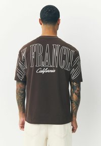 Brun bomulds T-shirt med hvid grafisk tekst, der står "SAN FRANCISCO California" i forskellige størrelser på ryggen, korte ærmer, afslappet pasform.