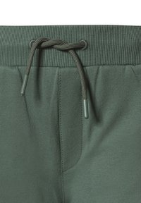 Zelené joggers kalhoty vyrobené z měkké tkaniny, s žebrovaným pasem, nastavitelnou šňůrkou s plastovými konci a bočními kapsami.