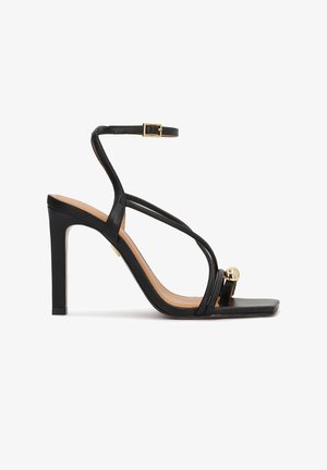 Black high-heeled sandal with ankle strap, slim toe loop featuring a gold ball accent, and a square open toe design.