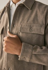 Harmaa villa-sekoite takki, jossa on kaksi nappikiinnitettyä rintataskua, näkyvät ompeleet ja kauluksellinen kaula-aukko. Takissa on rento istuvuus ja teksturoitu kangas.