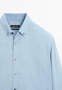 Himmelblaues Button-Up-Hemd aus strukturiertem Stoff. Verfügt über einen Kragen, eine Vorderfront mit Knöpfen und ein minimalistisches Design.