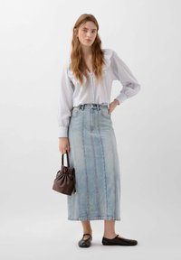 Gonna in denim azzurro chiaro con bottoni frontali, abbinata a una blusa bianca a quadri e una borsa in pelle marrone scuro. Ballerine nere completano il look.