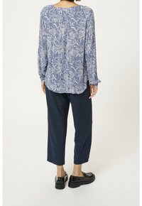 Camicia a maniche lunghe blu con motivo floreale bianco, abbinata a pantaloni a vita alta navy e scarpe con platform nere. Tessuto morbido e vestibilità rilassata.