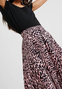 Černý top s krátkým rukávem doplněný růžovou sukní s černým leopardím vzorem, splývavý materiál a detail se staženým pasem.