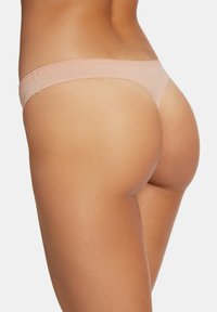 Huidskleurige stringonderbroek met een gladde textuur en een dunne band, voorzien van subtiele geribbelde accenten aan de tailleband.