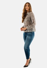 Blusa a maniche lunghe con motivo nelle tonalità crema e marrone, abbinata a jeans blu aderenti e tacchi alti neri, caratterizzata da un design casual.