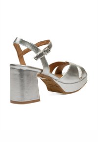 Sandalias de plataforma plateadas con tacón grueso, punta abierta, diseño de tiras cruzadas y correa ajustable en el tobillo. Textura metálica suave.