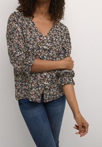 Svart blus med blommönster och V-ringning, med små blommor i flera färger, puffärmar och knapprad framtill. Matchas med blå jeans.