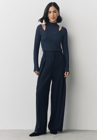 Top blu navy a maniche lunghe con dettagli a spalla scoperta, abbinato a pantaloni a vita alta a gamba larga in tessuto blu navy coordinato e scarpe nere con punta a punta.