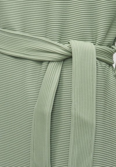 Ανοιχτό πράσινο υφασμάτινο ύφασμα με ραβδώσεις και ζώνη ίδιου χρώματος δεμένη σε κόμπο γύρω από την περιοχή της μέσης, που παρουσιάζει την υφή και τις λεπτομέρειες του ενδύματος.