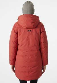 Parka aislante roja con capucha, que cuenta con un bolsillo trasero con cremallera y un logo negro en la parte superior de la espalda. Mangas largas con puños ajustables.