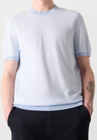 Camisa de punto de manga corta de color azul claro con escote redondo, puños y dobladillo acanalados en contraste. Textura suave, corte casual, diseño minimalista.