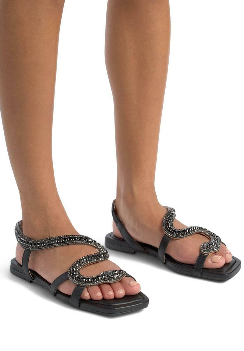 Schwarze Sandalen mit flacher Sohle und quadratischer Zehenpartie, mit einem dekorativen, gewellten Be strap aus Perlen über dem Rist.