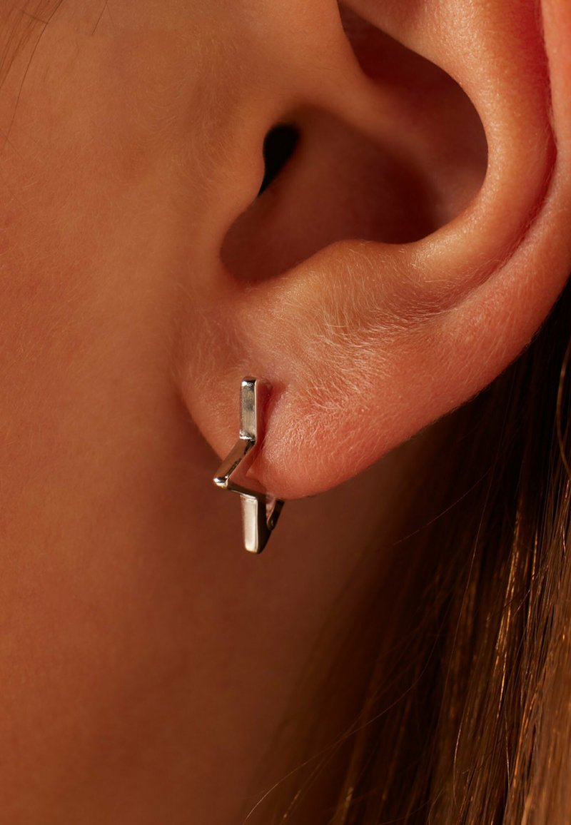 Silberne geometrische Ohrringe mit einem eleganten Design, das eine Zickzackform und eine glänzende Oberfläche aufweist, am Ohrläppchen getragen.
