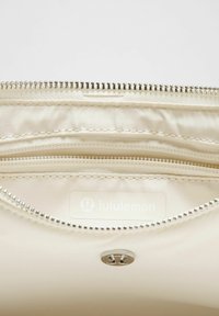 Beige dragkedjefodral med en sl�ät yta, silverfärgad dragkedja och inre fack. Lululemon-logotyp synlig på insidan.