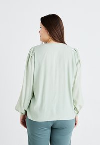 Mint green blouse with puffed long sleeves and a straight hem. Soft fabric with a smooth texture. Simple, no visible patterns or accents.