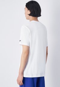 Witte katoenen t-shirt met korte mouwen, ronde hals en een klein logo op de mouw. Glad materiaal; ontspannen pasvorm.