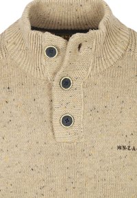 Beige gebreide trui met een gestructureerde afwerking, voorzien van een geribbelde kraag, drie donkere knopen en spikkels van geel en grijs door de stof.