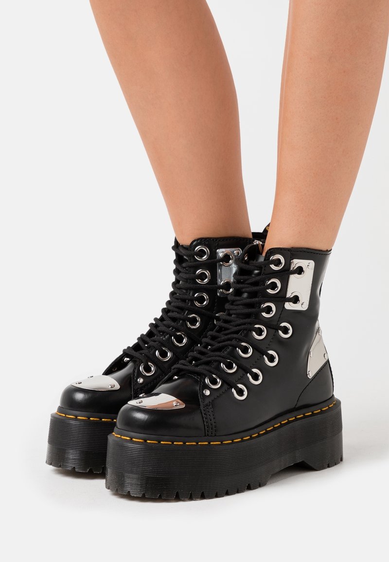 Botas de combate de plataforma negras con acentos metálicos, punta redonda y diseño con cordones. Presentan herrajes plateados y suela de goma texturizada.