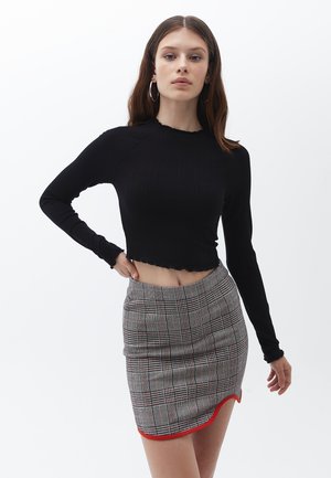 Zwarte ribbel crop top met lange mouwen, met een golvende zoom; gecombineerd met een grijze geruite minirok met rode rand en een getailleerde pasvorm.
