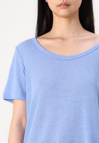 Tricou scurt cu mânecă scurtă, de culoare albastru deschis, cu un gât adânc în formă de cupă, realizat dintr-un material moale, având un croi lejer și o textură netedă.