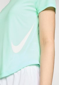 Svetlo modra športna majica s kratkimi rokavi, opremljena z belim Nike swoosh logotipom na strani in skrajšanim dizajnom. Gladka tekstura tkanine.
