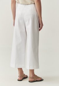 Pantaloni bianchi a gamba larga con una texture liscia, dotati di tasche posteriori e vita alta. Abbinati a sandali piatti beige.