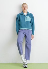 Fleece pullover in teal with a light blue chest pocket, paired with light purple trousers and white sneakers with gray accents.