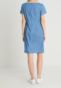 Lyhythihainen, polvipituinen sininen mekko pehmeästä kankaasta, jossa on yksinkertainen leikkaus ja takana vetoketjukiinnitys. Yhdistetty valkoisiin tennareihin.