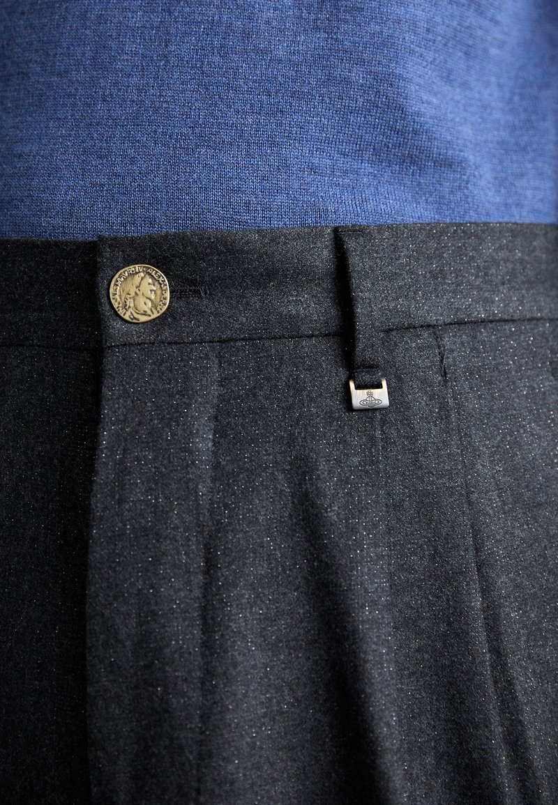 Pantaloni neri con una trama sottile, dotati di un dettaglio con bottone in bronzo e un piccolo emblema in metallo argentato, abbinati a una camicia blu a trama.