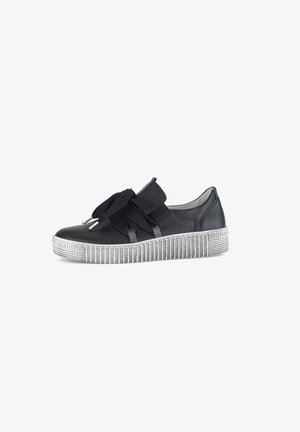 Zwarte leren sneaker met dikke witte geribbelde zool en grote zwarte stoffen strikdetails aan de zijkant.