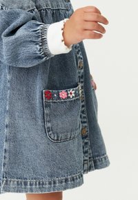 Jeanskleid mit Puffärmeln, Knopfleiste und einer Tasche mit floralen Stickereien in Pink, Rot und Weiß. Klassische blaue Denim-Textur.